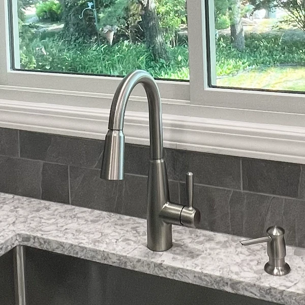 kitchen faucet and built-in soap dispenser on granite countertop in front of window
