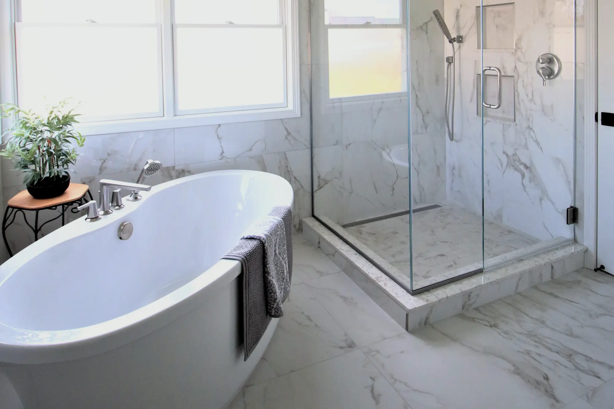 A standalone bathroom tub, glass shower and marble tile floors and walls.