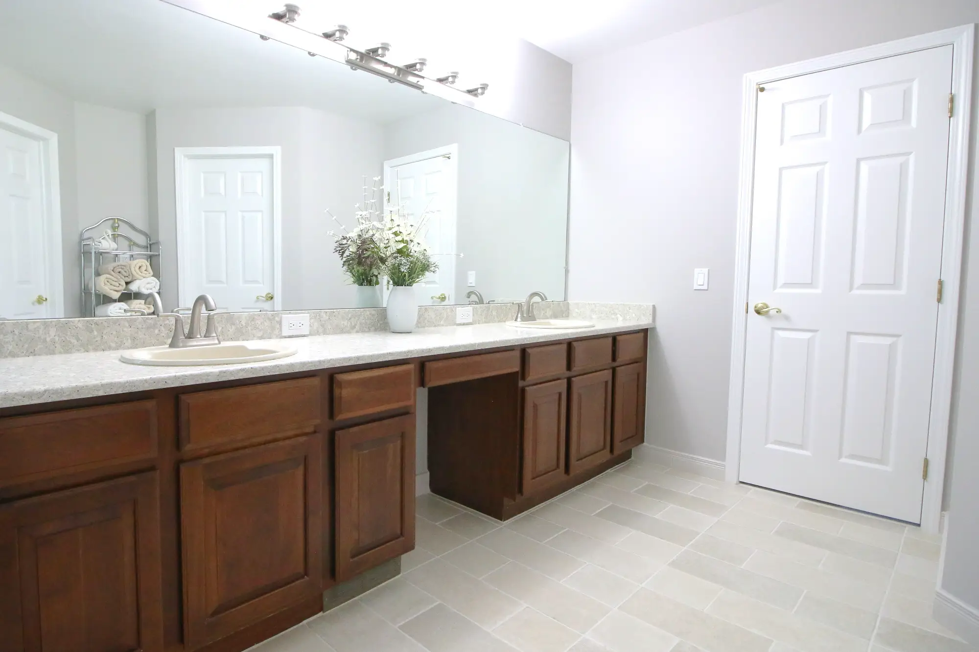 A renovated bathroom vanity with a large mirror, dual sinks and medium tone wood cabinets.