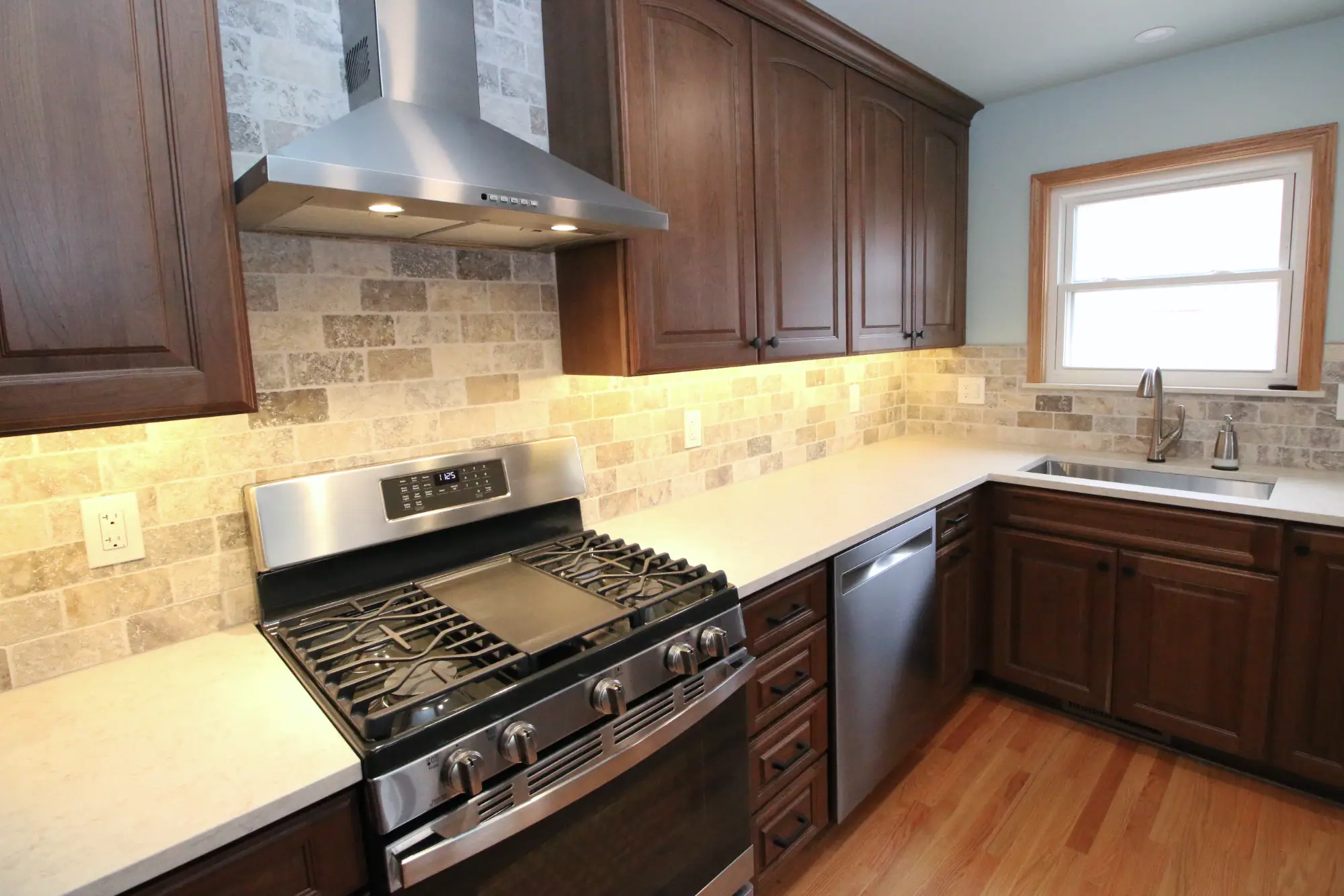 A kitchen remodel with dark wood cabinets, stone backspash and light stone counters.